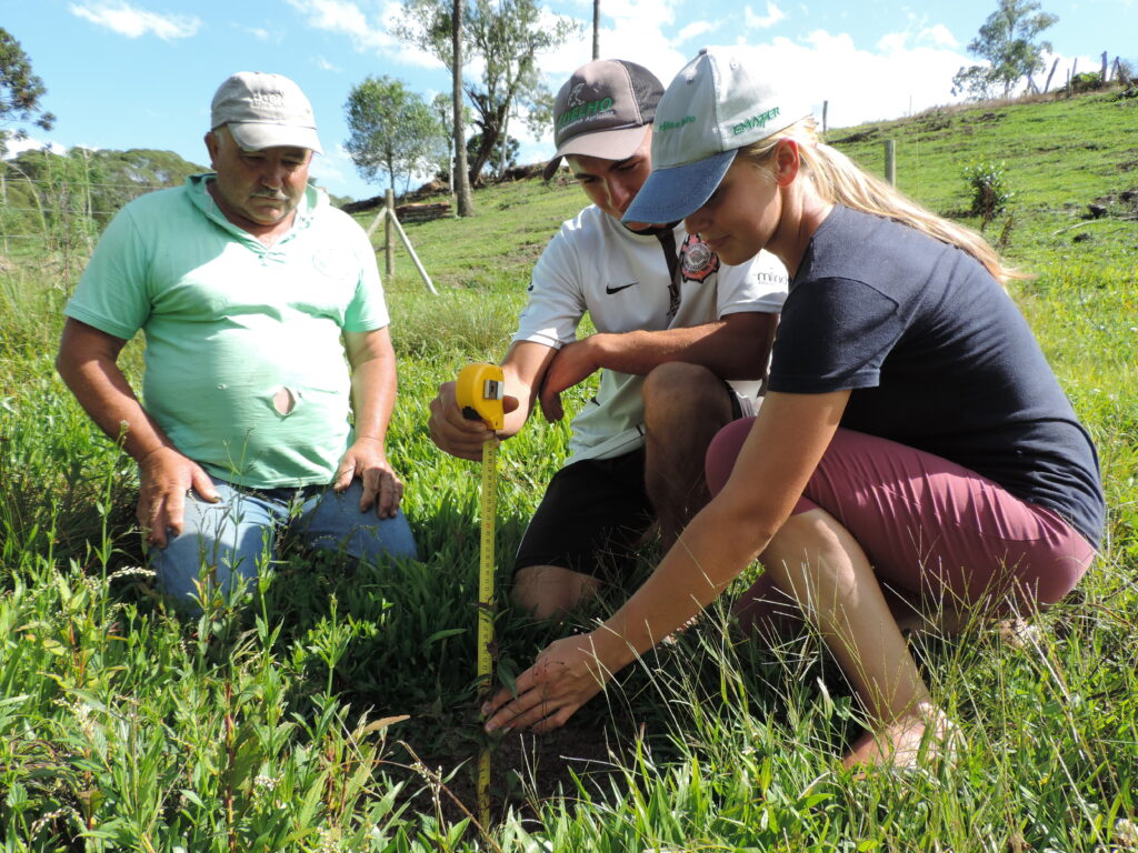 Imagem de três pessoas sentadas a grama e uma delas segura fita métrica.