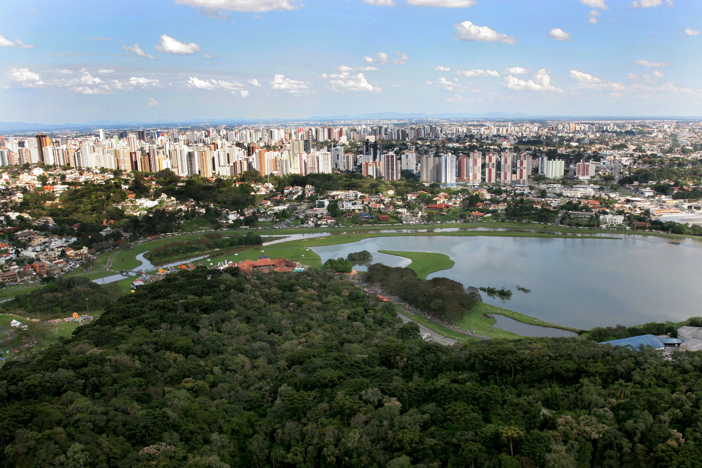 Imagem aérea de Curitiba, com prédios e lagos.