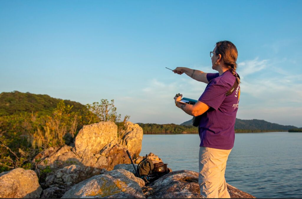 Imagem de uma pessoa apontando na direção das pedras na beira à mar.