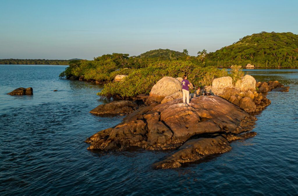Imagem aérea de um pessoa em cima de pedras na beira no mar.