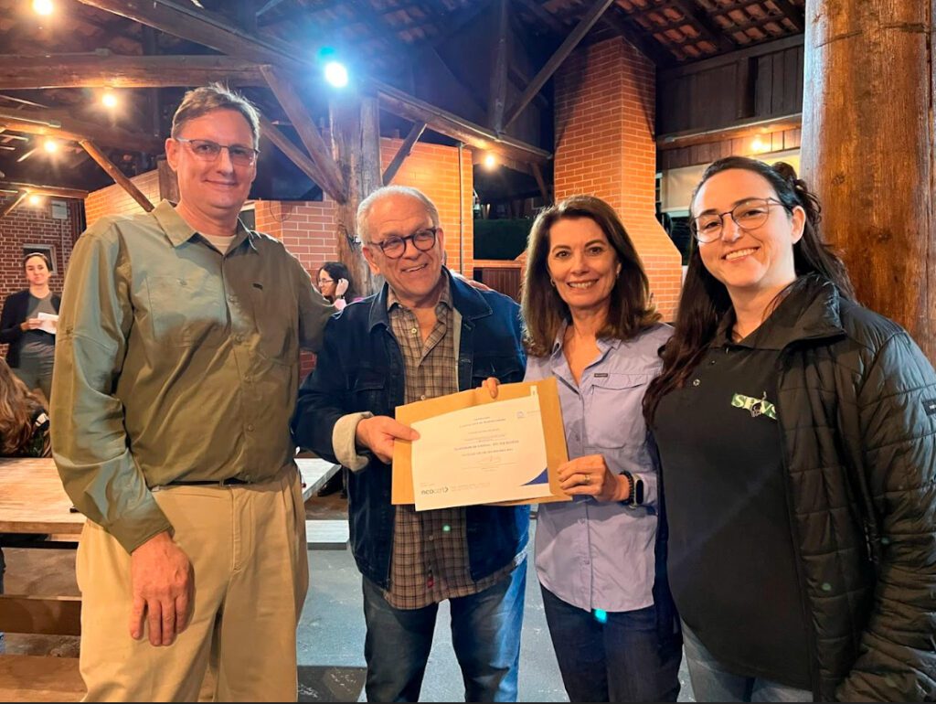 Imagem de quatro pessoas sorrindo para a foto e segurando um documento.