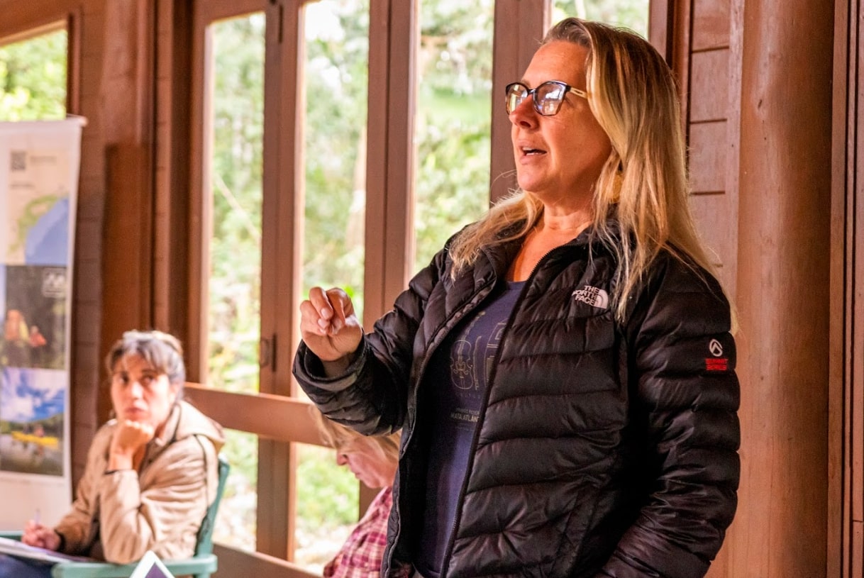 Imagem de Solange Latenek, uma mulher loira de cabelos lisos e de óculos, que está vestindo um casaco preto.