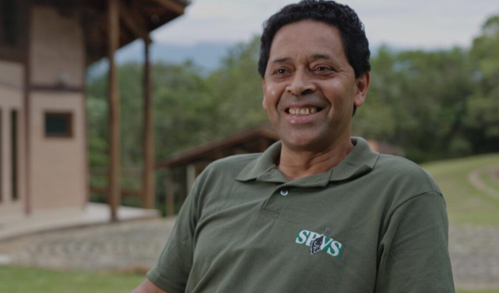 Imagem de um homem negro de pela clara, cabelo curto e escuro, usando camiseta da SPVS sorrindo para a câmera.