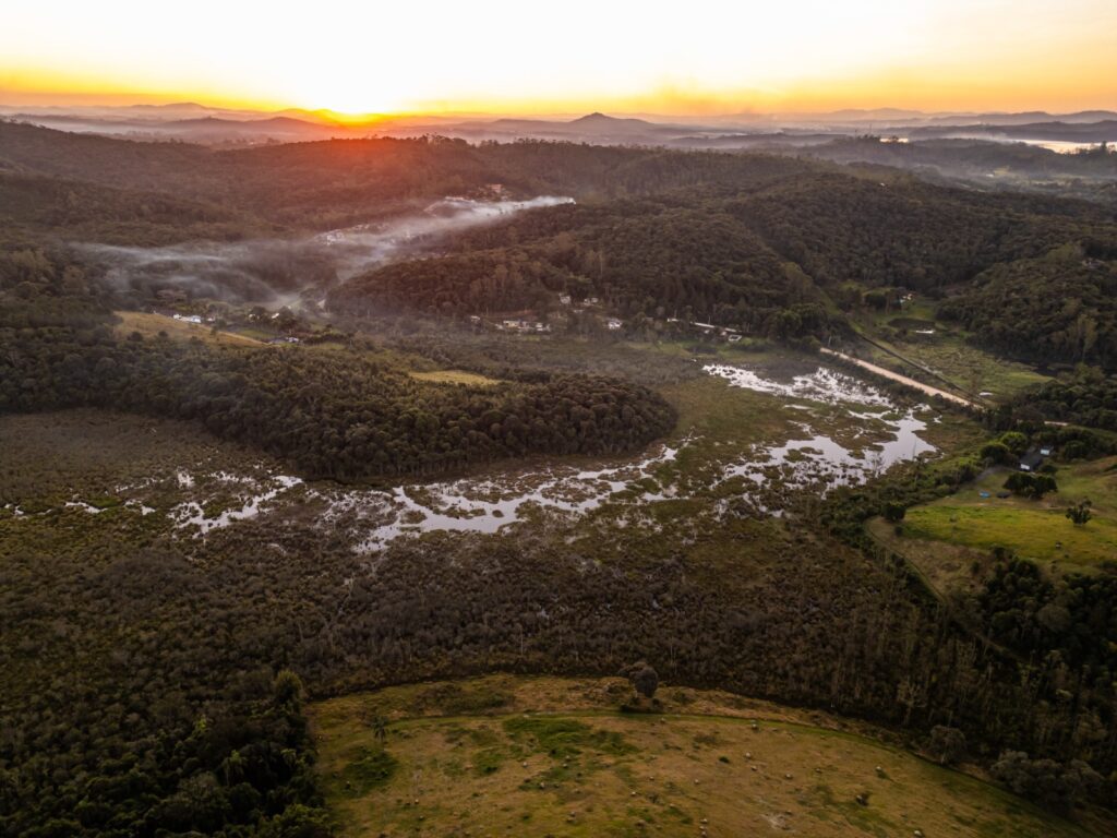 Imagem aérea de montanhas verdes e céu ao nascer do sol.