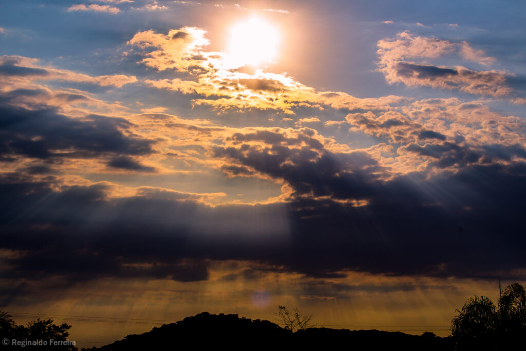 Imagem de pôr do sol com nuvens e montanhas ao fundo.