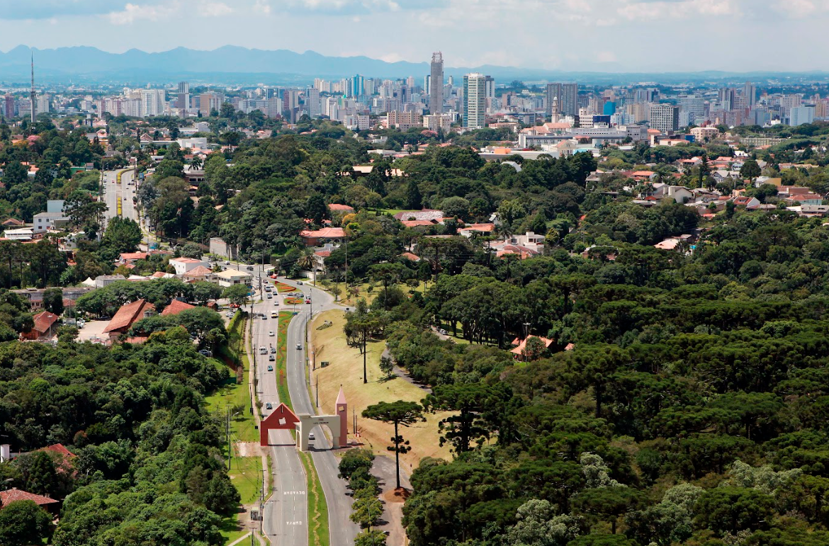 Imagem aérea da cidade de Curitiba, Paraná. Com avenida e árvores.