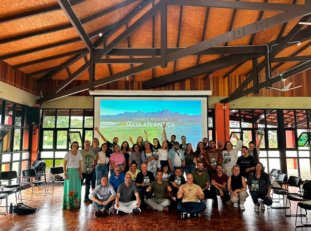 Imagem com 36 pessoas posando para a foto, com um projetor ao fundo.